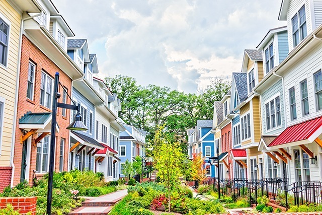 Row Of Colorful, Red, Yellow, Blue, White, Green Painted Residential Townhouses, Homes, Houses With Brick Patio Gardens In Summer