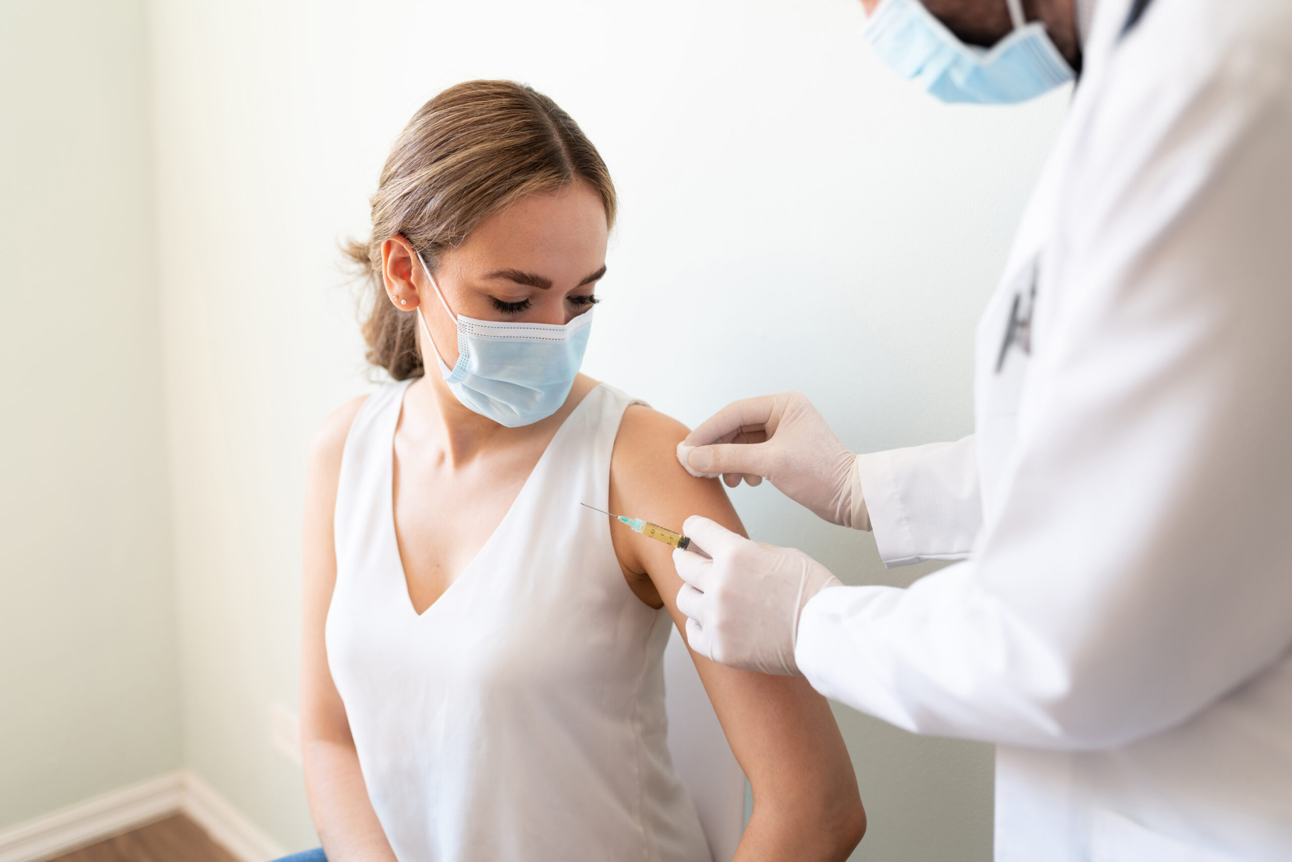 Doctor Using A Cotton Swab With Alcohol To Clean A Woman's Arm Before Applying A Vaccine In A Doctor's Office