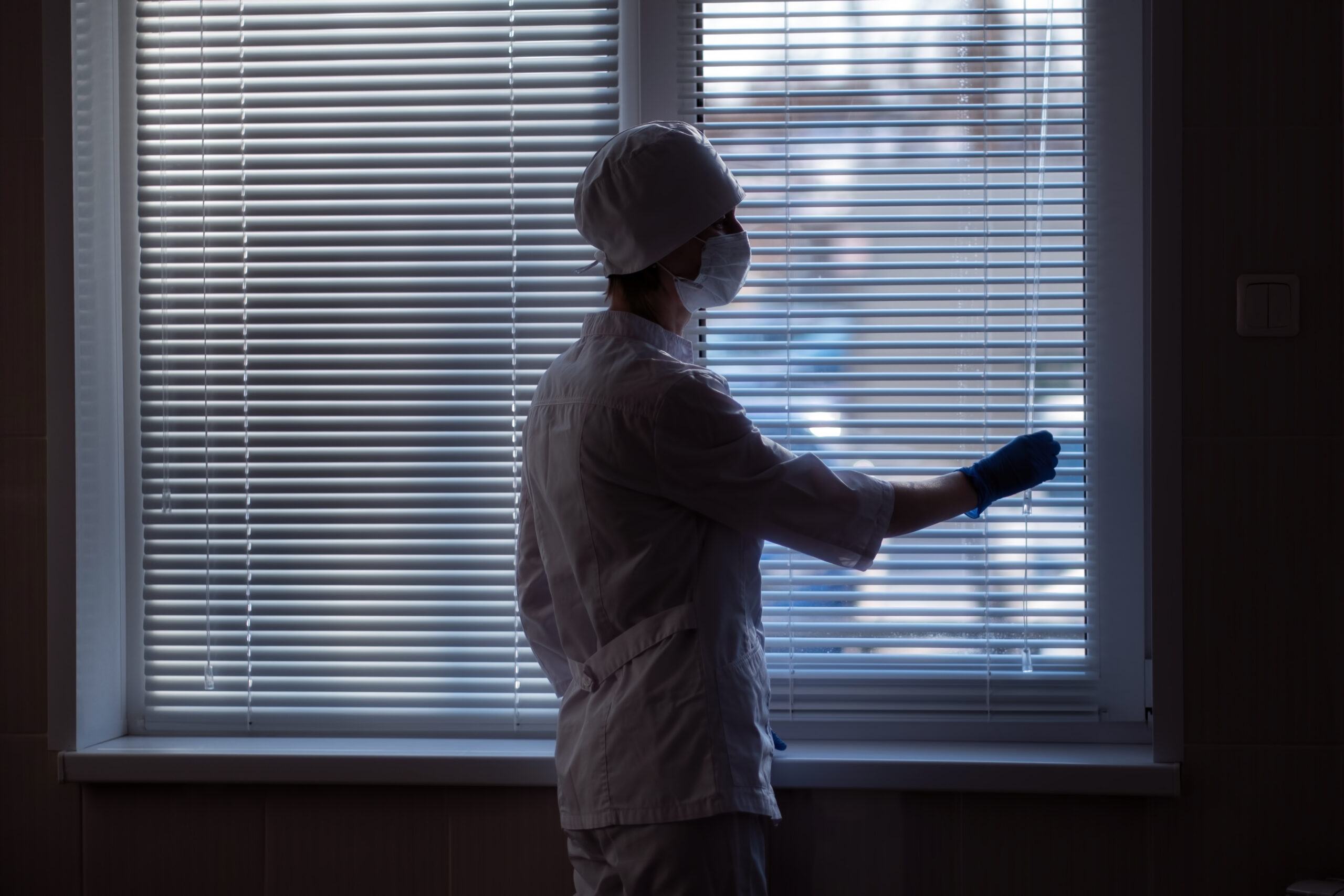 A Female Doctor Closes The Blinds On A Window In A Hospital, Rear View.